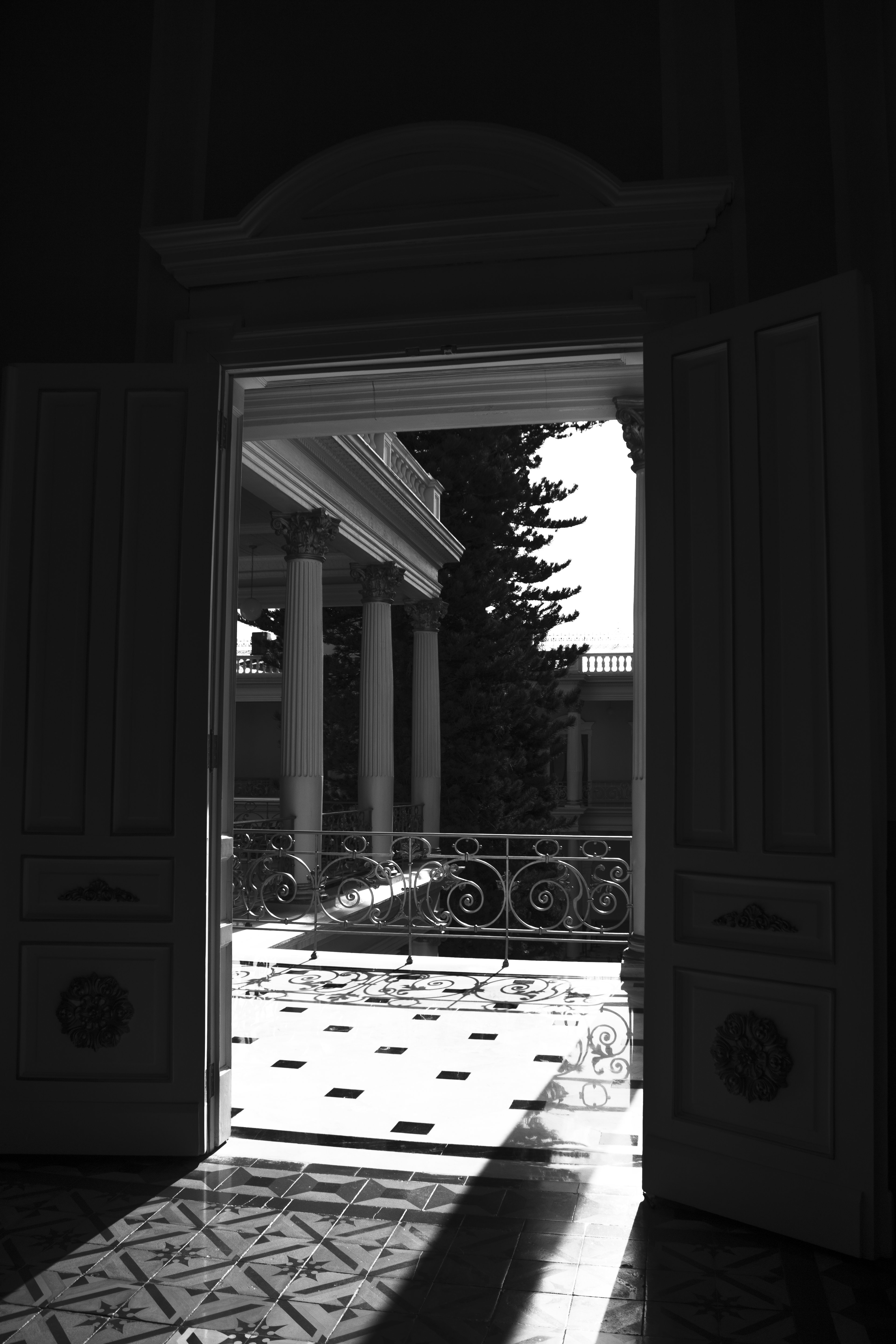 Puertas abiertas hacia un balcón con columnas y luz diagonal
