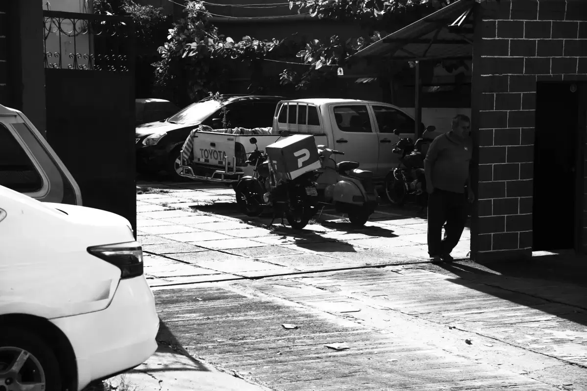 Estacionamiento con camioneta, motos y un hombre apoyado en la pared