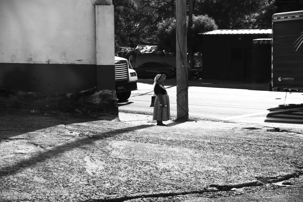 Mujer en esquina soleada junto a un poste y camiones