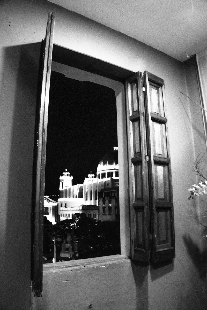 Catedral iluminada de noche vista desde una ventana con contraventanas