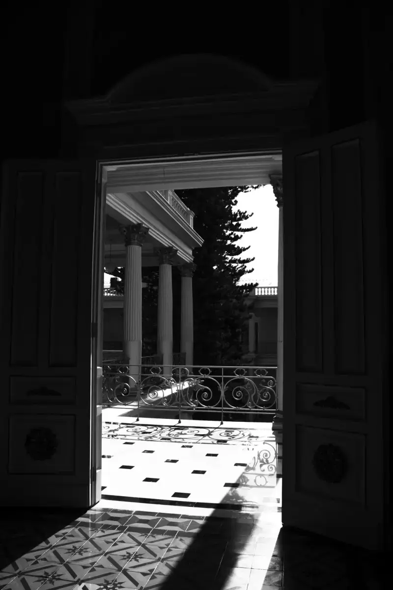 Puertas abiertas hacia un balcón con columnas y luz diagonal
