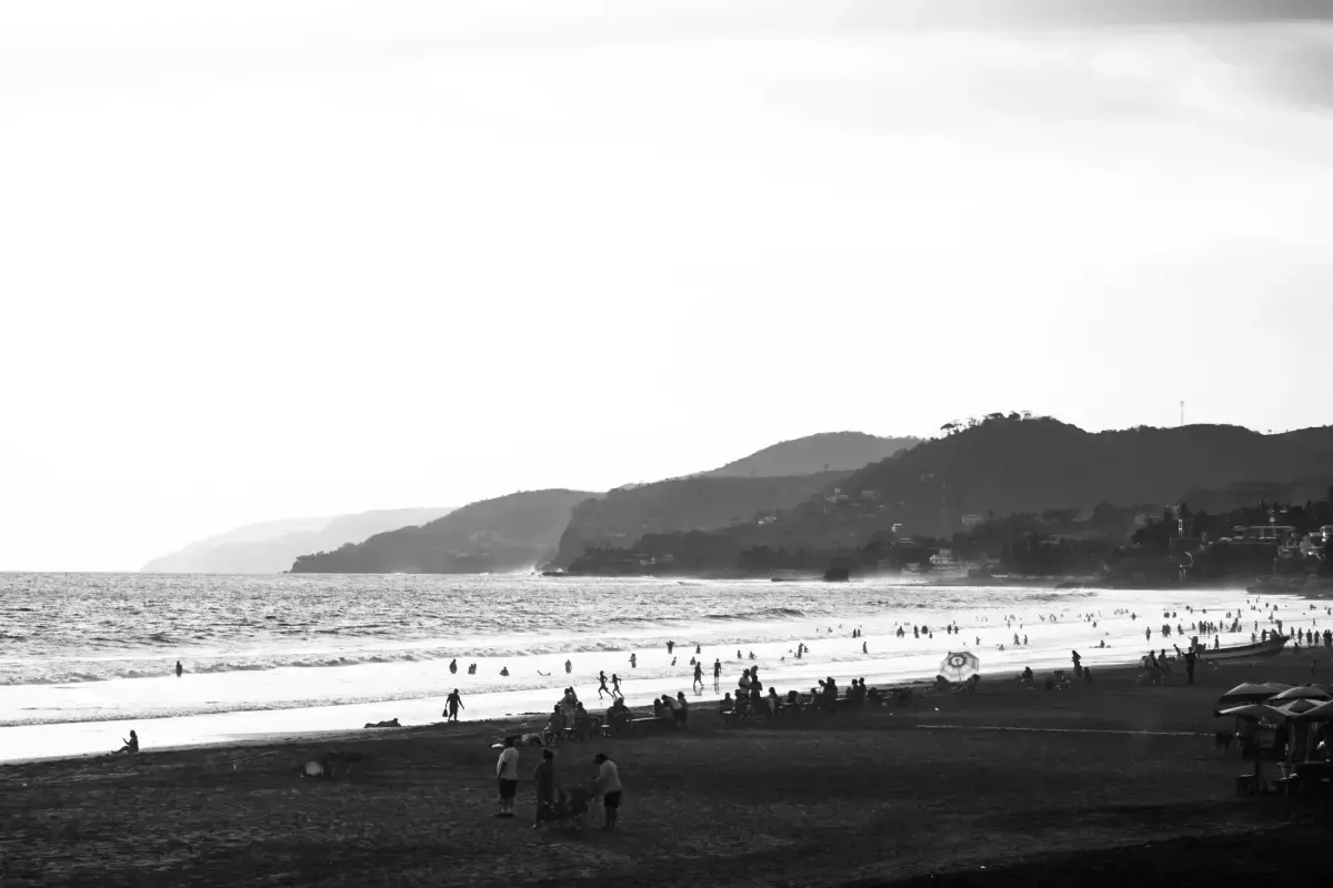 Playa abarrotada con siluetas frente al mar y cerros