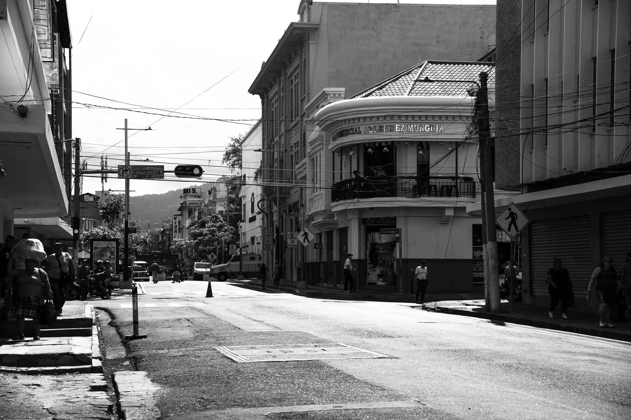 Esquina urbana con peatones, cableado y fachada curva bajo luz intensa